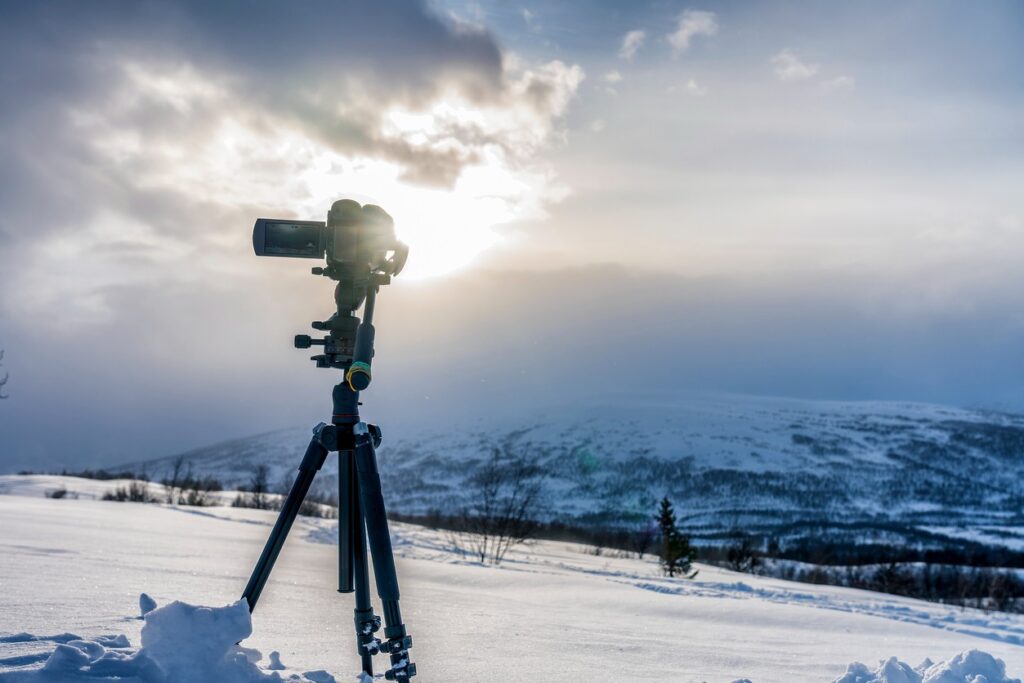 A camera sits on a tripod outdoors in winter in Bend, Oregon with mountains in the background. 